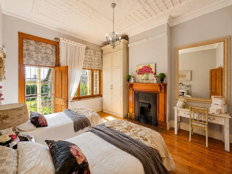A charming bedroom featuring original timber flooring, an ornate ceiling, and a classic cast iron fireplace with a timber mantel.