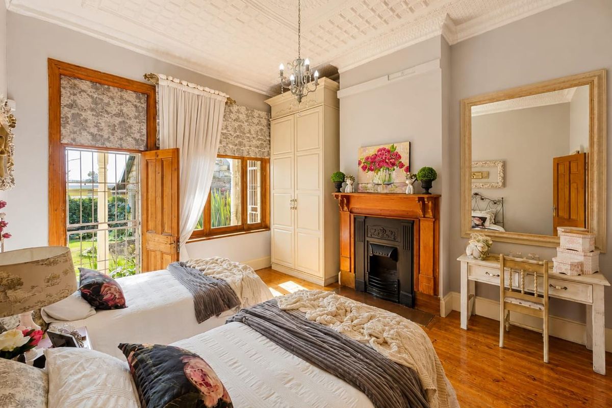 A charming bedroom featuring original timber flooring, an ornate ceiling, and a classic cast iron fireplace with a timber mantel.