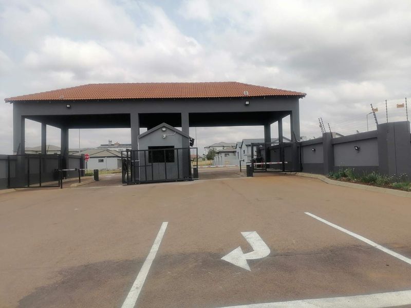 A well-maintained residential estate entrance featuring a secure gatehouse, perimeter walling with electric fencing, and a paved driveway with boom gate access.