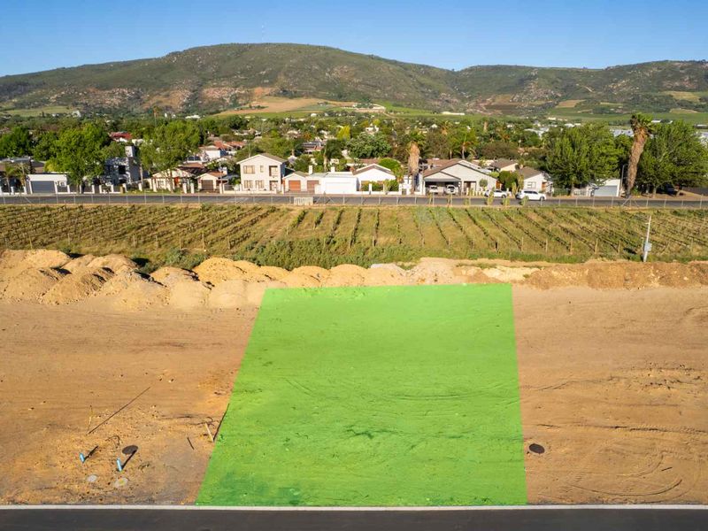 Aerial view of a vacant residential plot with utility connection points, situated in a developed neighborhood with mountain views.