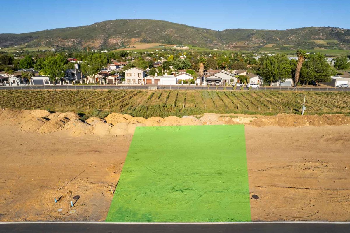 Aerial view of a vacant residential plot with utility connection points, situated in a developed neighborhood with mountain views.