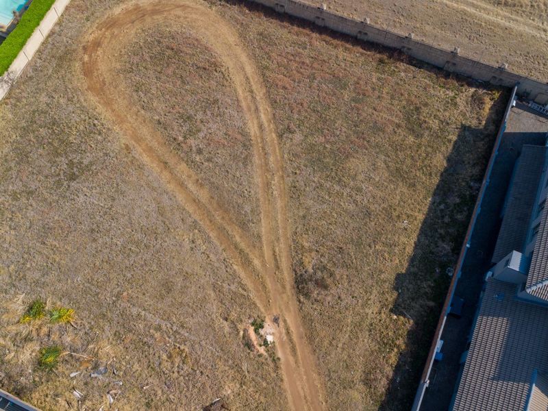 Aerial view of a vacant residential plot featuring a perimeter wall and an existing dirt driveway path.