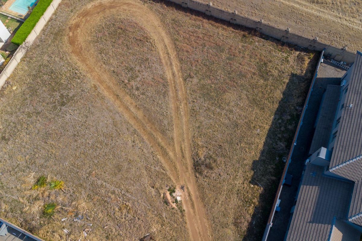 Aerial view of a vacant residential plot featuring a perimeter wall and an existing dirt driveway path.
