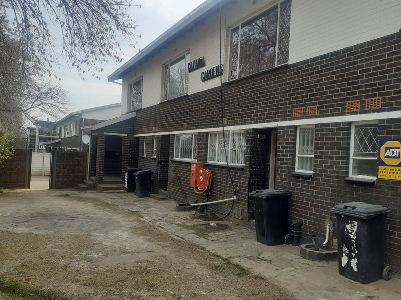 Exterior view of the Gazania Gardens apartment complex featuring a brick facade, security bars on windows, and a paved entrance area.