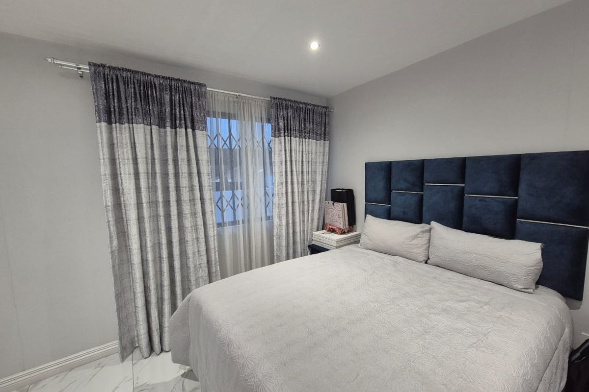 A well-maintained bedroom featuring modern tiled flooring, recessed downlighting, and a window fitted with security bars.