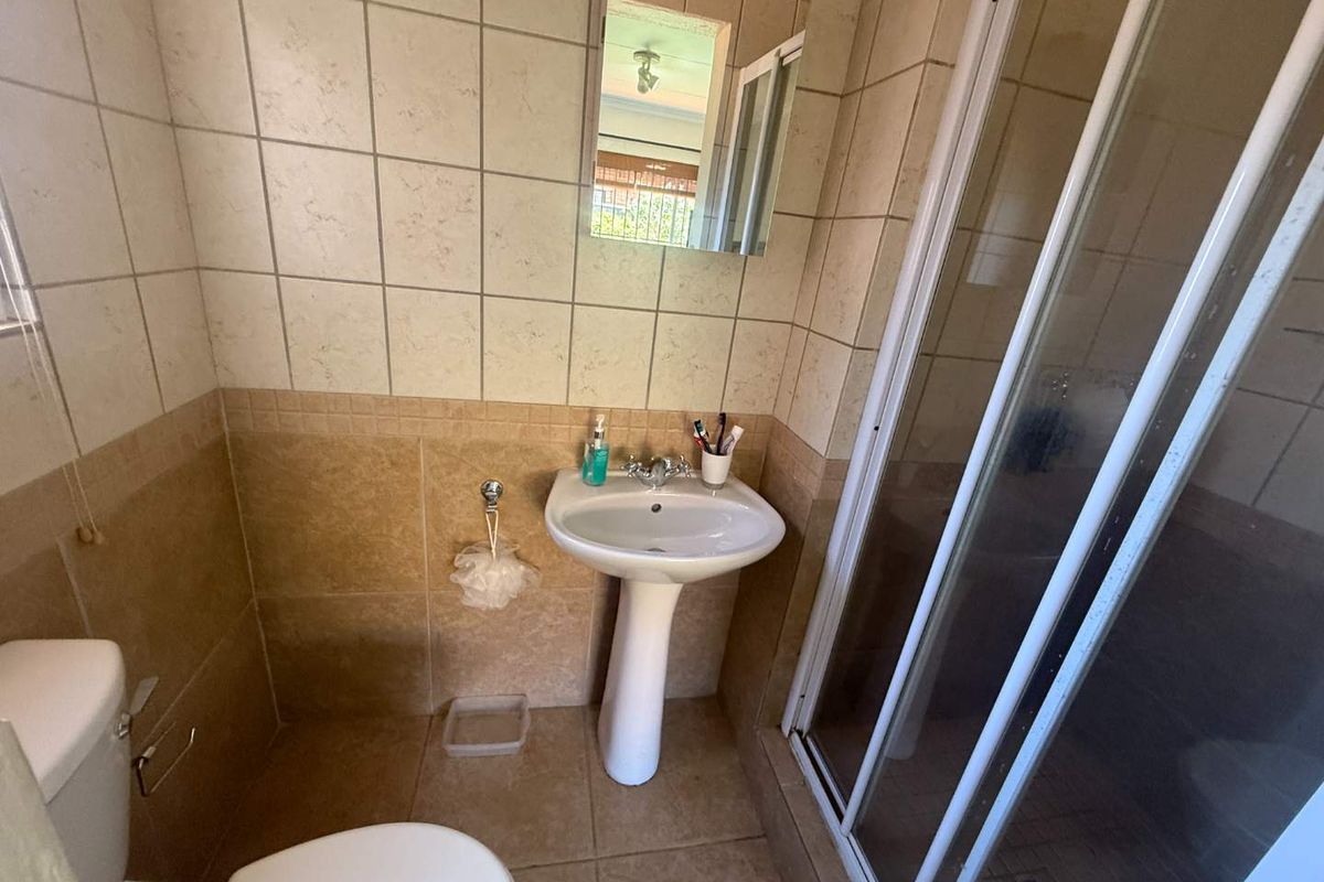 A functional bathroom featuring a pedestal sink, a shower enclosure with sliding doors, and neutral wall and floor tiling.