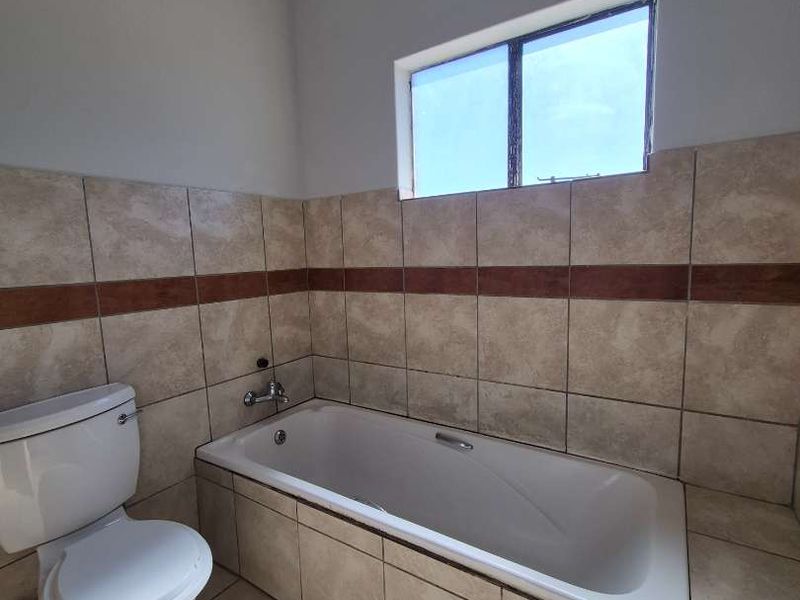 A functional bathroom featuring a built-in bathtub, ceramic wall and floor tiling, and a standard toilet.