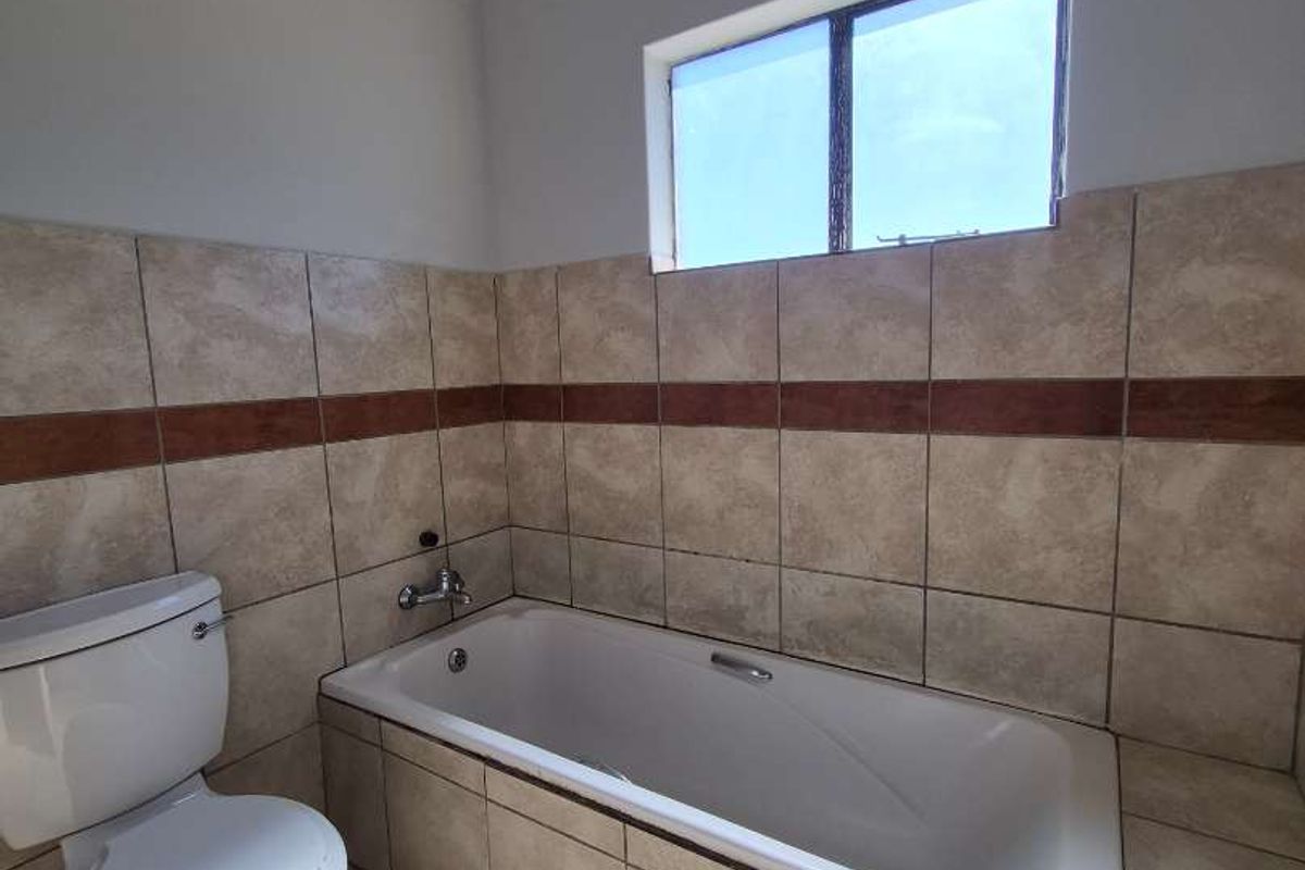 A functional bathroom featuring a built-in bathtub, ceramic wall and floor tiling, and a standard toilet.