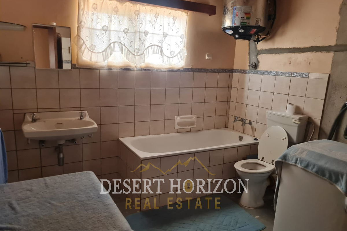 A dated bathroom featuring a standard bathtub, wall-mounted basin, and toilet, with visible plumbing and unfinished wall sections requiring renovation.