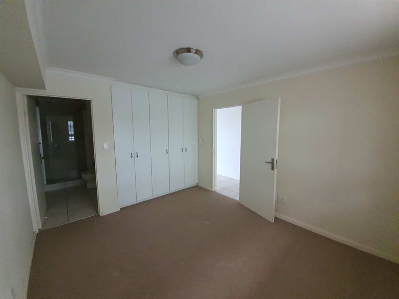 An empty bedroom featuring neutral carpet flooring, built-in cupboards, and direct access to an en-suite bathroom.
