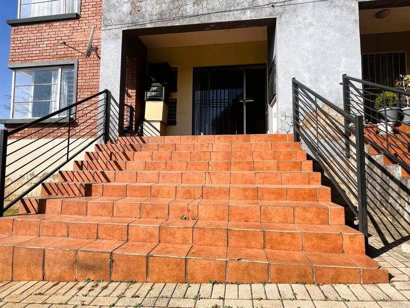 Front entrance of the townhouse featuring a tiled staircase with metal railings and a security gate, showing signs of exterior wear and maintenance needs.