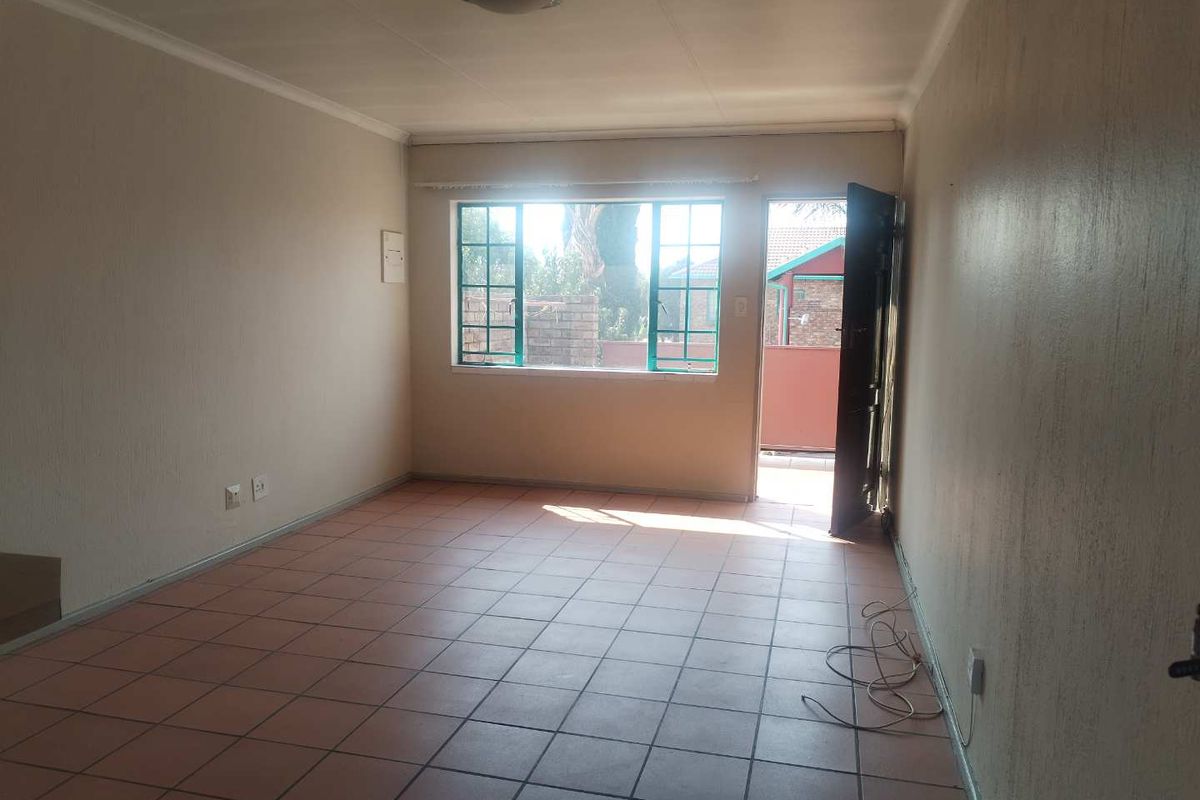 An empty living room featuring tiled flooring, a ceiling light, and direct access to an outdoor area through a security door.