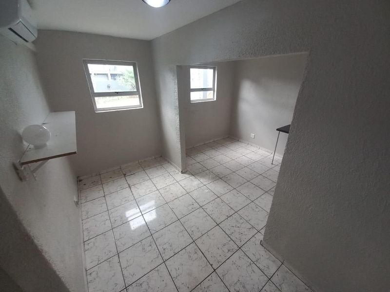 An empty open-plan living area featuring tiled flooring, a wall-mounted air conditioning unit, and neutral wall finishes.