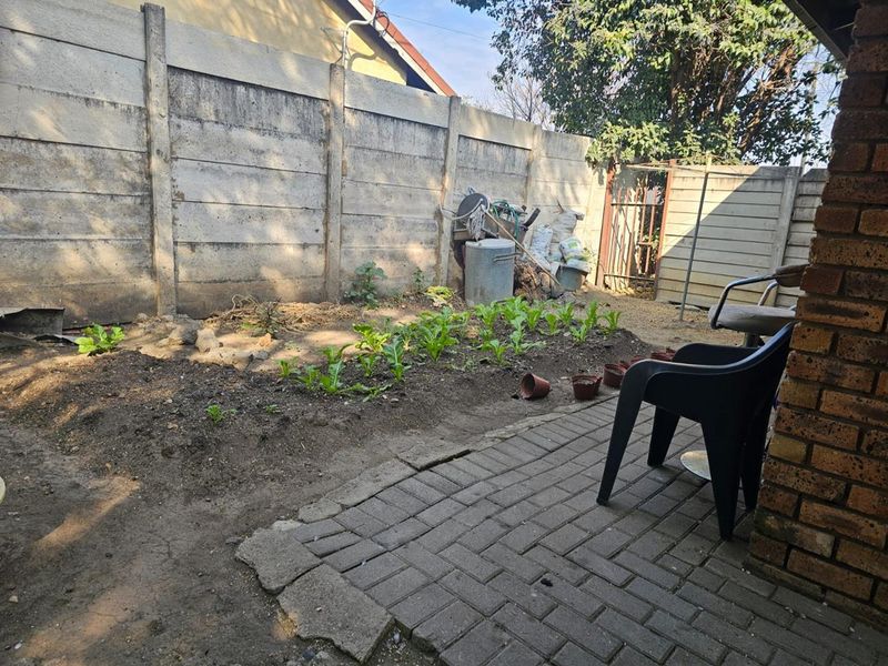 A rear garden area featuring a paved patio, a precast concrete boundary wall, and a small vegetable patch.