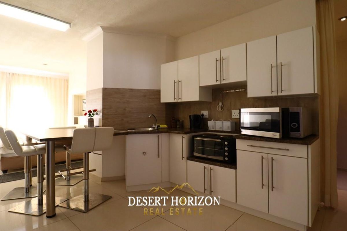 Compact kitchen area featuring white cabinetry, laminate countertops, and a built-in sink, seamlessly integrated into an open-plan living space.