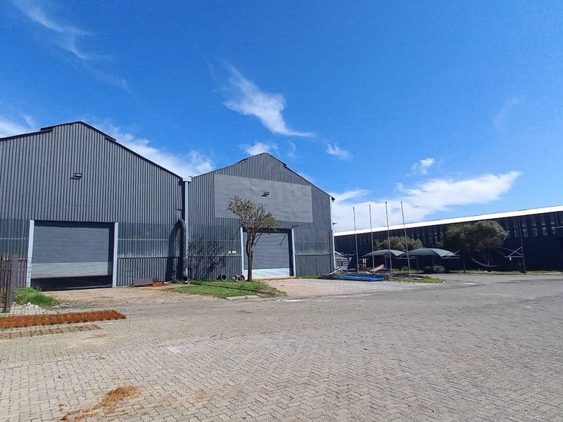 Industrial property featuring large corrugated metal warehouse structures with roller shutter doors, set within a spacious paved yard with security fencing.