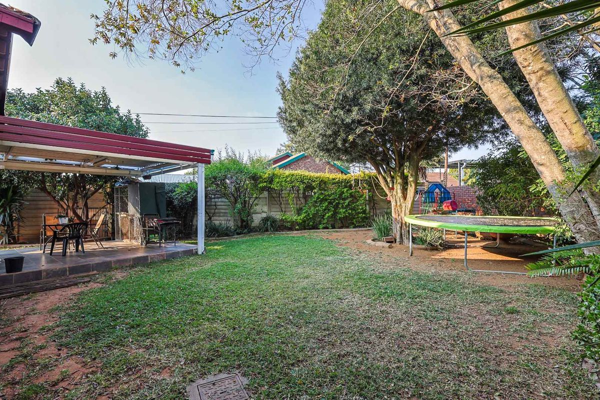 A private rear garden featuring a covered patio area, established trees, and a lawn, providing a functional outdoor space for relaxation and recreation.