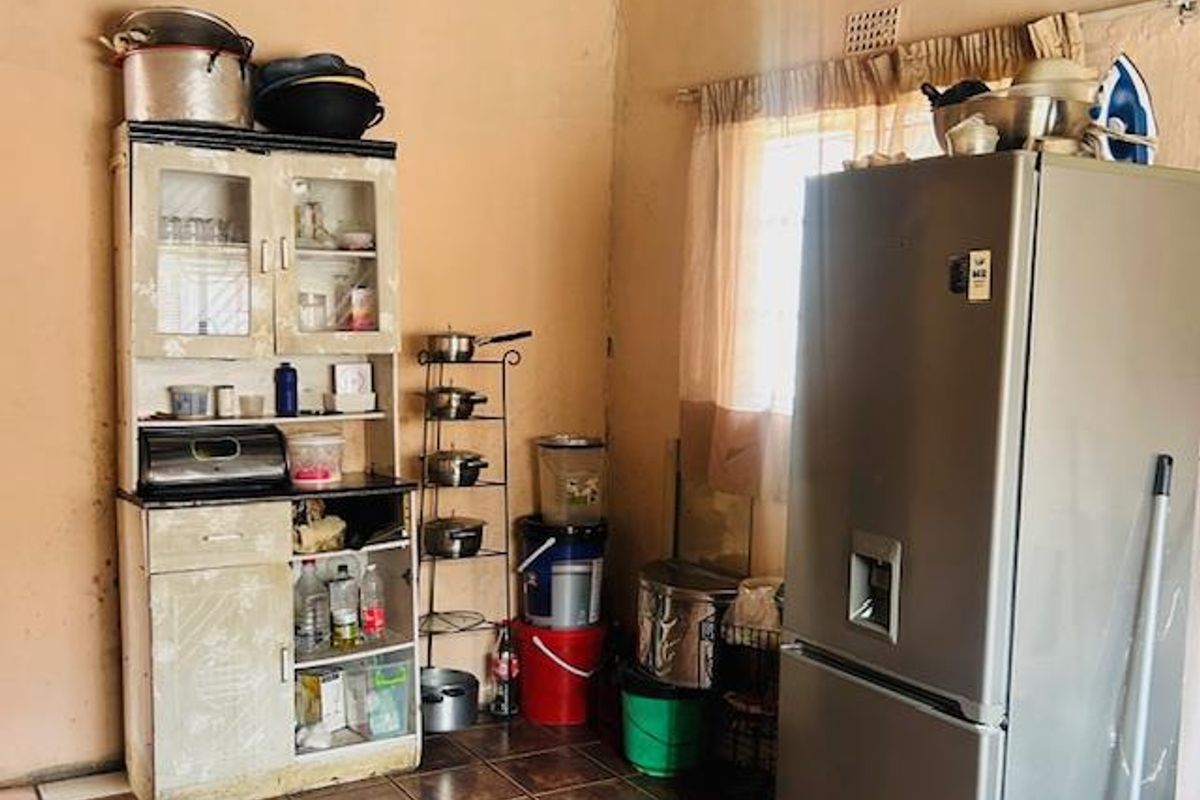 A functional kitchen area featuring tiled flooring and exposed ceiling beams, currently requiring cosmetic updates and wall refinishing.