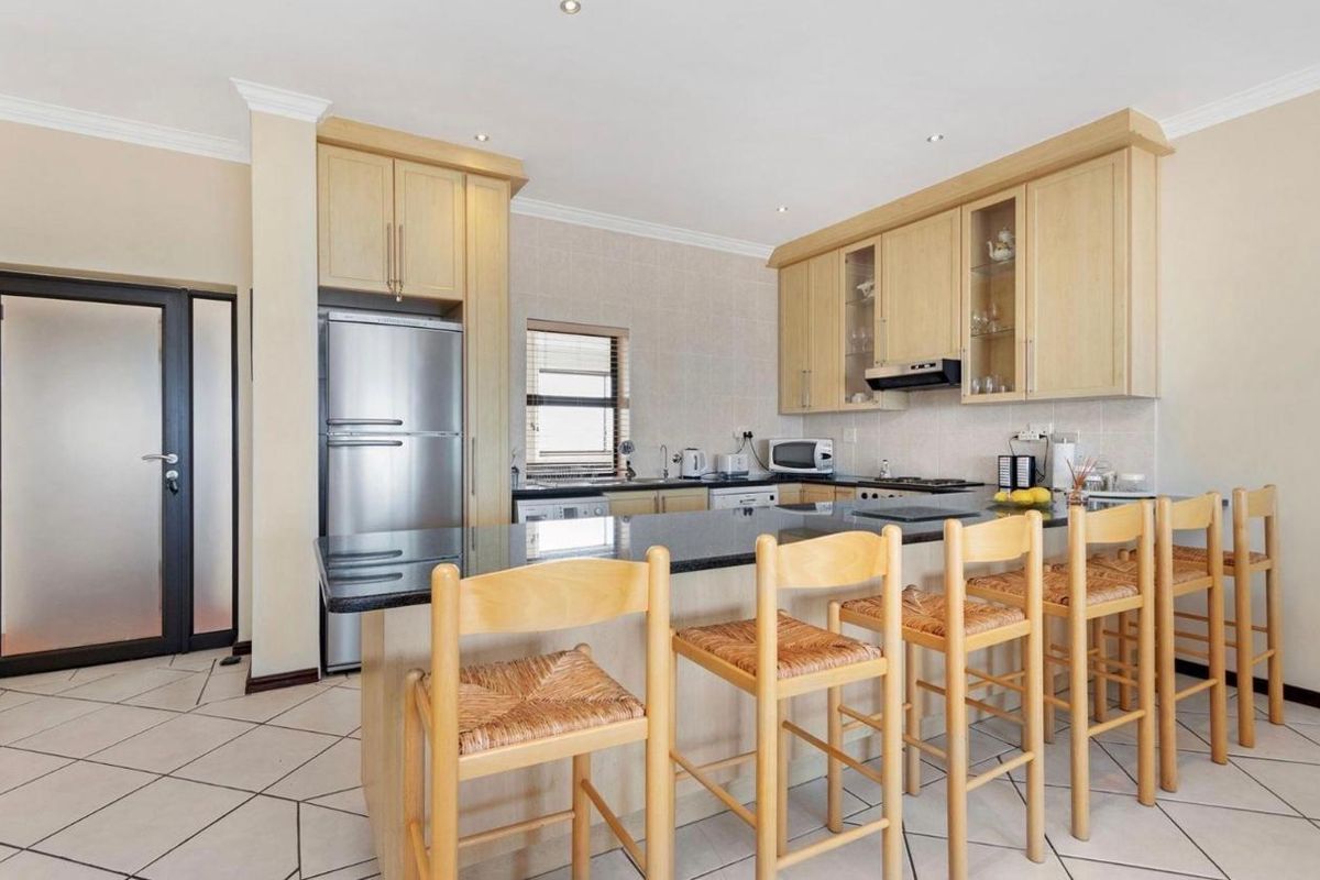 A functional kitchen featuring light wood cabinetry, granite countertops, a breakfast bar, and integrated appliances, set against tiled flooring.