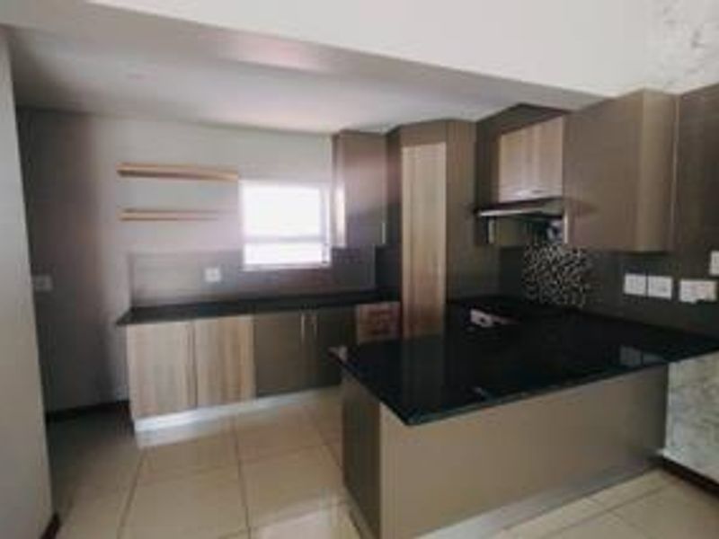 Modern kitchen featuring sleek built-in cabinetry, dark granite countertops, an integrated extractor fan, and neutral tiled flooring in an open-plan layout.