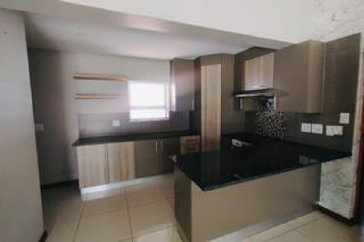 Modern kitchen featuring sleek built-in cabinetry, dark granite countertops, an integrated extractor fan, and neutral tiled flooring in an open-plan layout.