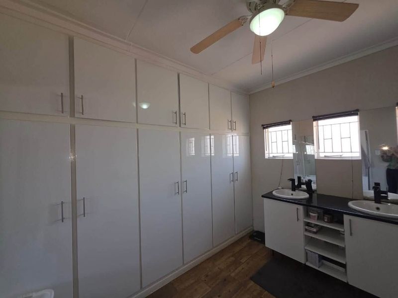 A well-maintained bathroom featuring extensive built-in cabinetry, a double vanity with modern fixtures, and a ceiling fan.
