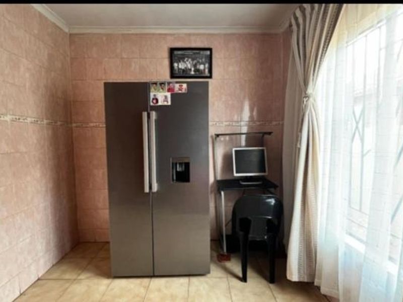 A kitchen area featuring full-height ceramic wall tiling, tiled flooring, and a window fitted with security bars.