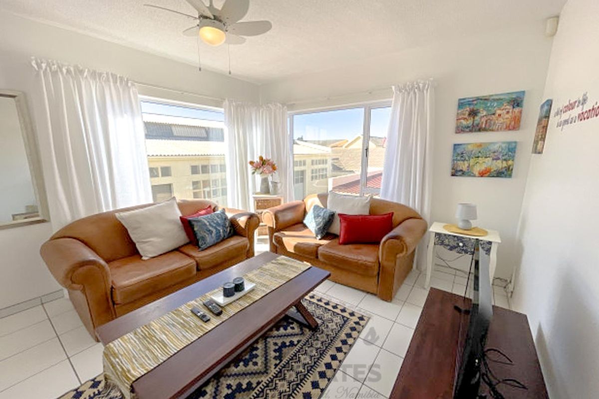 A bright living room featuring large windows, tiled flooring, and a ceiling fan, offering a comfortable and well-lit space for relaxation.