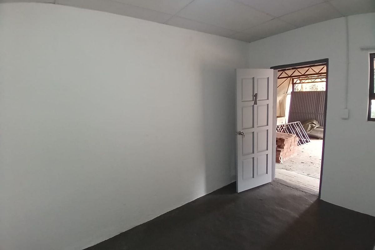 An empty, basic interior room featuring plain white walls, a simple panel door, and unfinished concrete flooring, leading to an outdoor construction area.