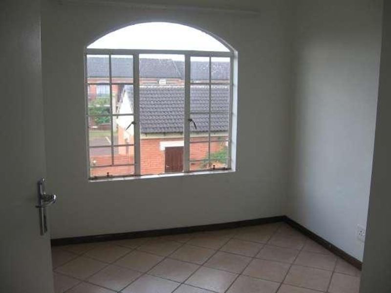 An empty bedroom featuring tiled flooring and a large arched window with views of the surrounding townhouse complex.