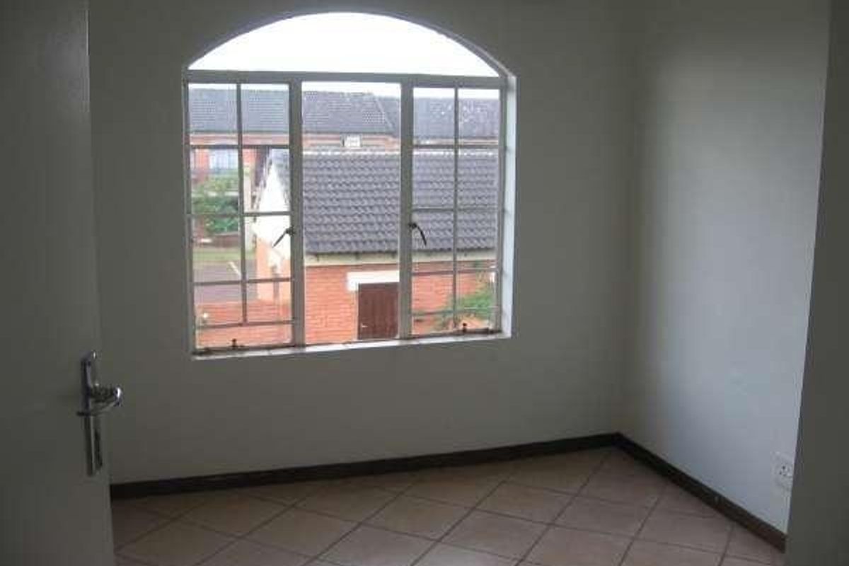 An empty bedroom featuring tiled flooring and a large arched window with views of the surrounding townhouse complex.