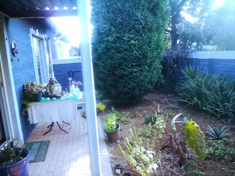 A covered patio area adjacent to a garden with a paved floor and boundary wall, offering a private outdoor space.