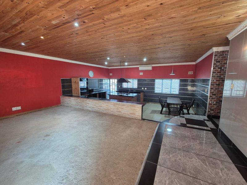 Spacious open-plan living and kitchen area featuring a timber ceiling, exposed brick accents, and a central kitchen island with built-in appliances.