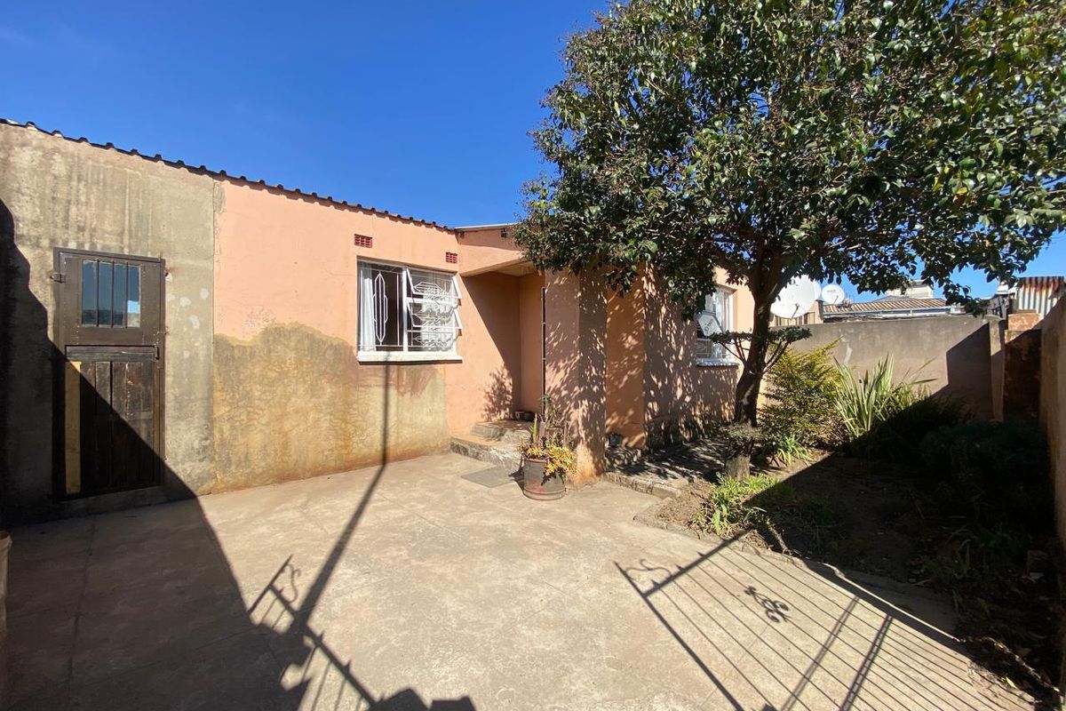 Rear exterior view of the property featuring a concrete patio area, security gates, and weathered exterior wall finishes requiring maintenance.