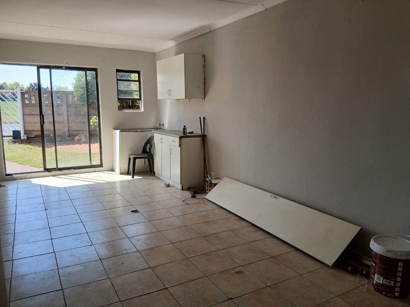 A basic kitchen area featuring tiled floors, built-in cabinetry with a sink, and a sliding glass door providing access to the rear garden.
