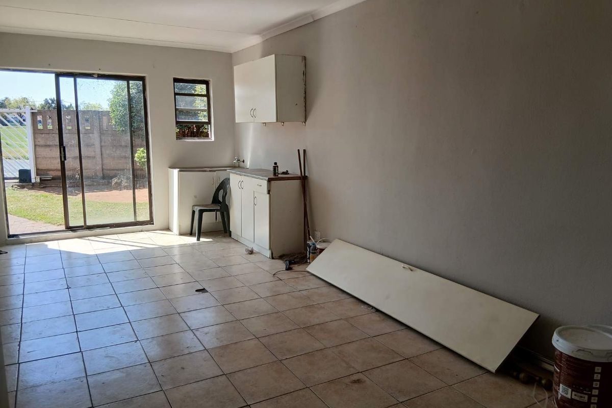 A basic kitchen area featuring tiled floors, built-in cabinetry with a sink, and a sliding glass door providing access to the rear garden.