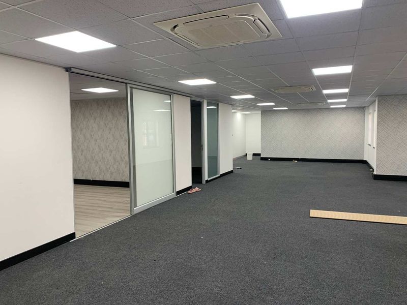 Spacious open-plan office area featuring a suspended ceiling with integrated LED lighting, cassette air conditioning, and a modern sliding glass partition.