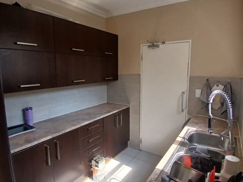 A functional scullery featuring dark wood cabinetry, laminate countertops, a double bowl stainless steel sink with a gooseneck mixer, and tiled flooring.