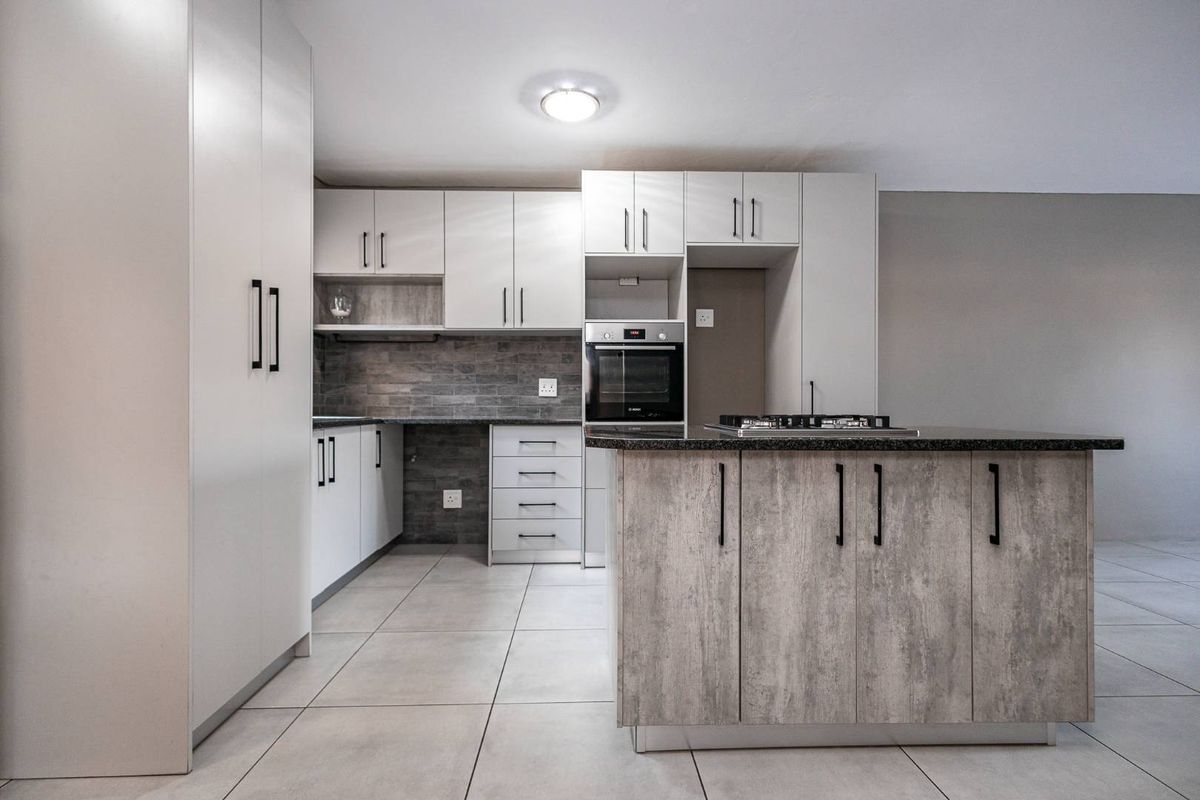 Modern kitchen featuring light-toned cabinetry, a central island with a built-in hob, integrated oven, and tiled flooring throughout.