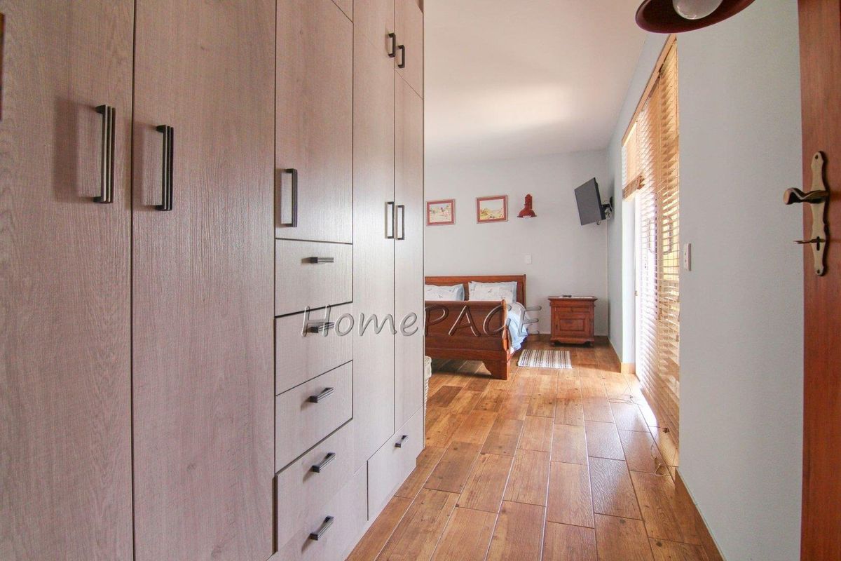 Bedroom featuring built-in wooden cabinetry, wood-look tile flooring, and large windows with fitted blinds, providing a warm and functional living space.