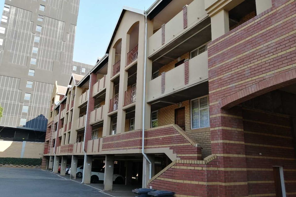 Exterior view of a multi-story apartment complex featuring face brick facade, covered ground-level parking, and private balconies with metal railings.