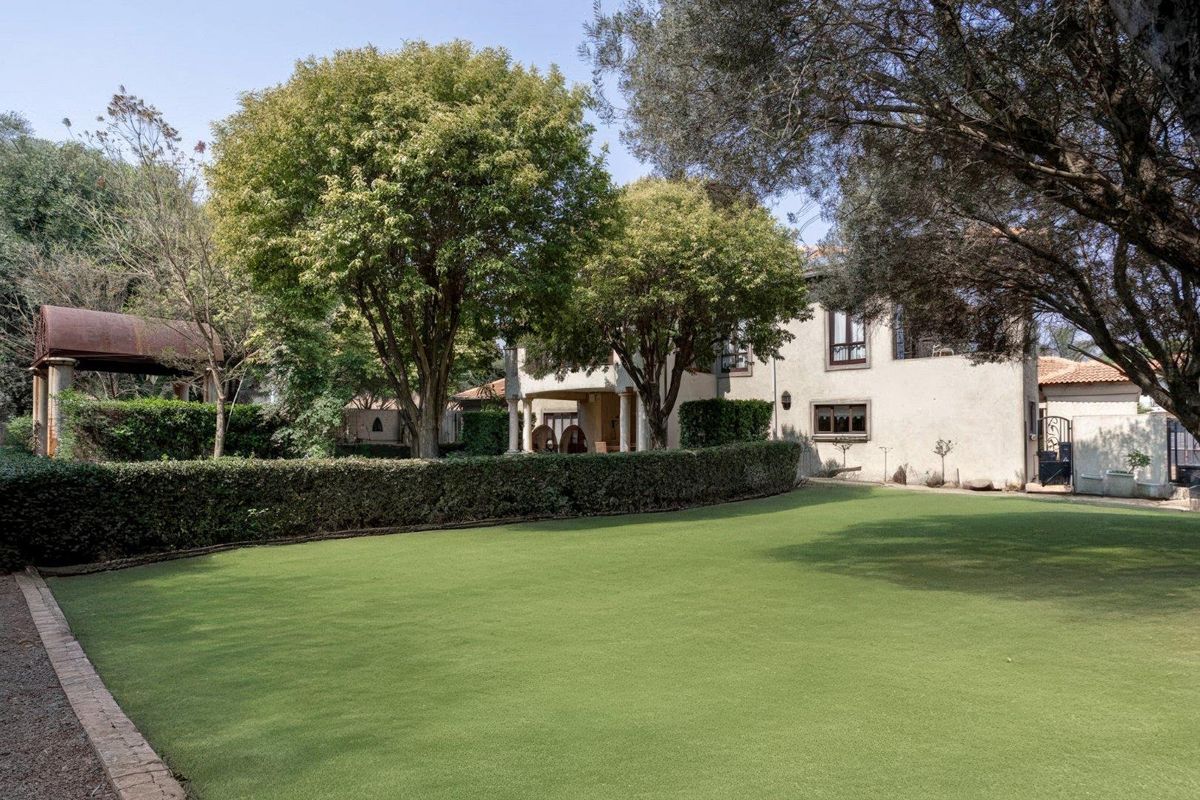 A well-maintained rear garden featuring a manicured lawn, mature trees, and a view of the property's rear facade and covered patio area.