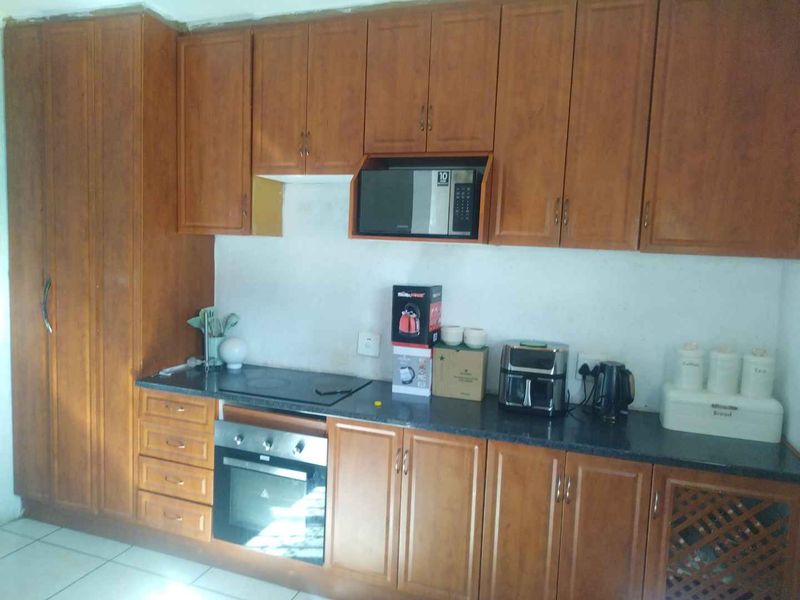 A functional kitchen featuring wood-finish cabinetry, integrated oven and hob, and dark countertops, offering a practical layout with potential for cosmetic updates.