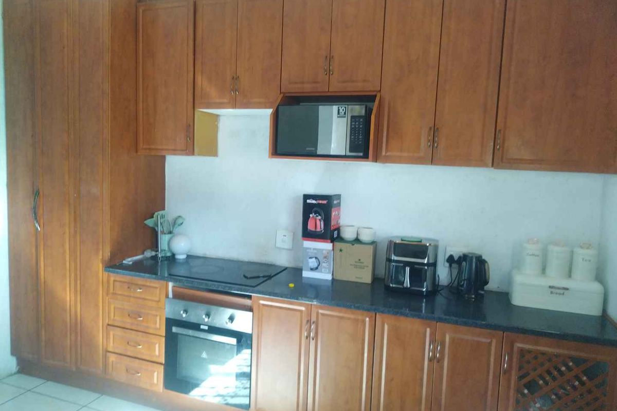 A functional kitchen featuring wood-finish cabinetry, integrated oven and hob, and dark countertops, offering a practical layout with potential for cosmetic updates.