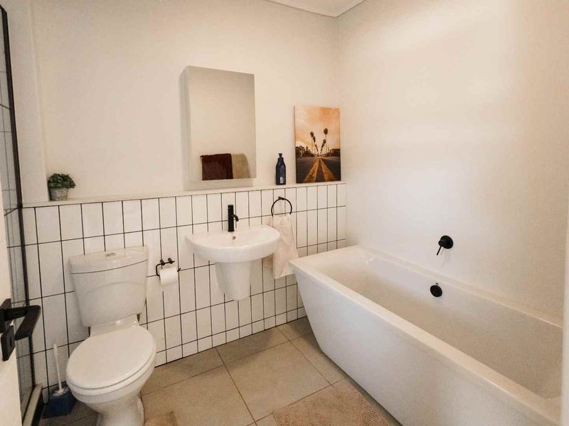 Modern bathroom featuring a freestanding bathtub, wall-mounted basin, and contemporary black matte fixtures with clean white tiled splashbacks.