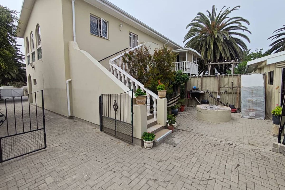 Exterior view of the property featuring a paved courtyard, external staircase with balustrades, and access to the upper level.