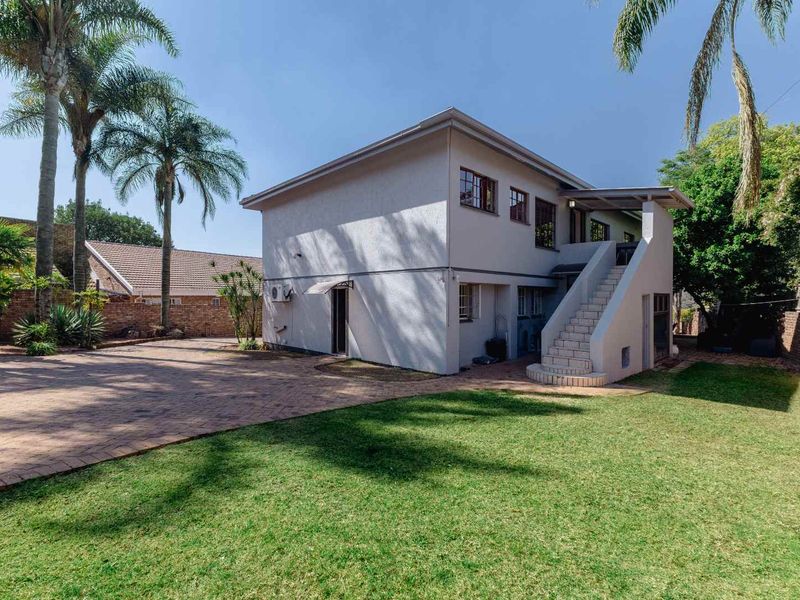 Rear view of the property featuring a paved driveway, a well-maintained lawn, and an external staircase leading to the upper level.