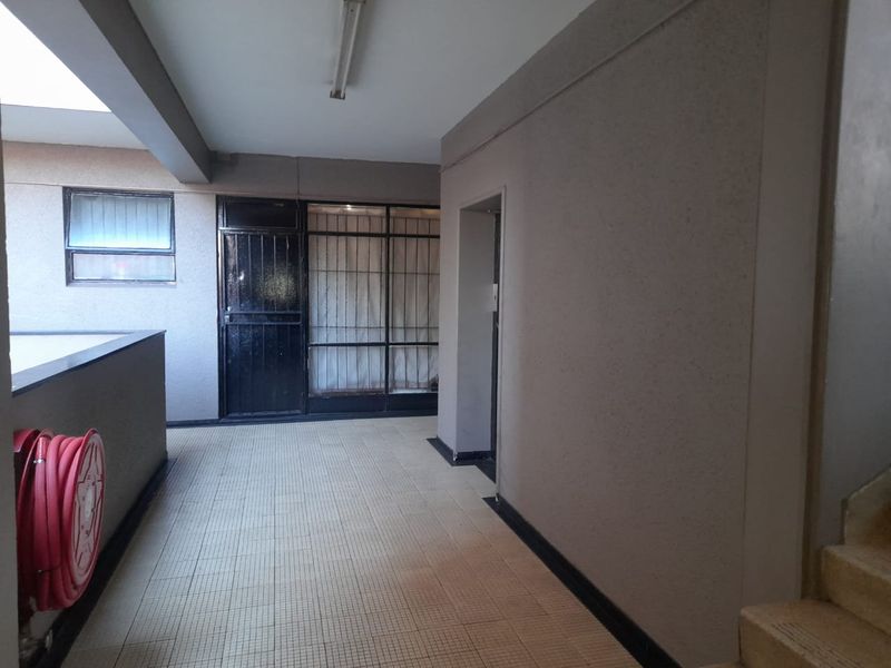 A functional apartment building hallway featuring tiled flooring, a fire hose reel, and secure access points.