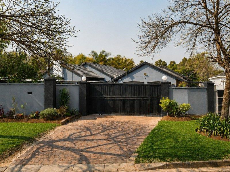 Front view of the property featuring a secure perimeter wall, gated entrance, paved driveway, and well-maintained garden area.