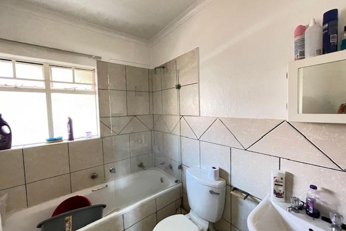 A functional bathroom featuring a bathtub with a glass shower screen, a pedestal basin, and a toilet, with visible signs of wear and ceiling staining.